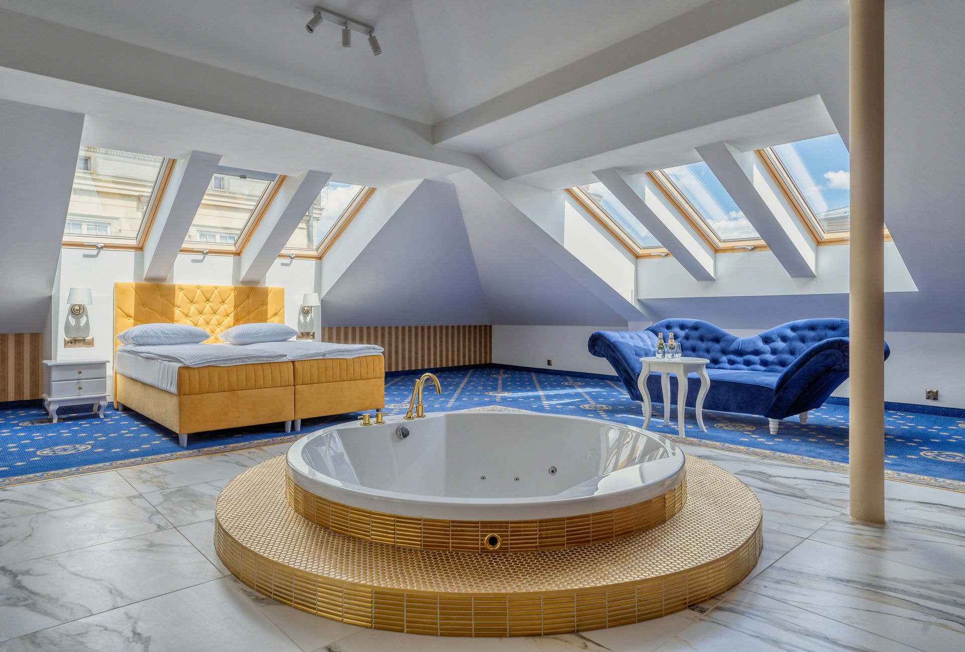 Luksusowa sypialnia na poddaszu z jacuzzi, żółtym łóżkiem i niebieską sofą pod oknami dachowymi