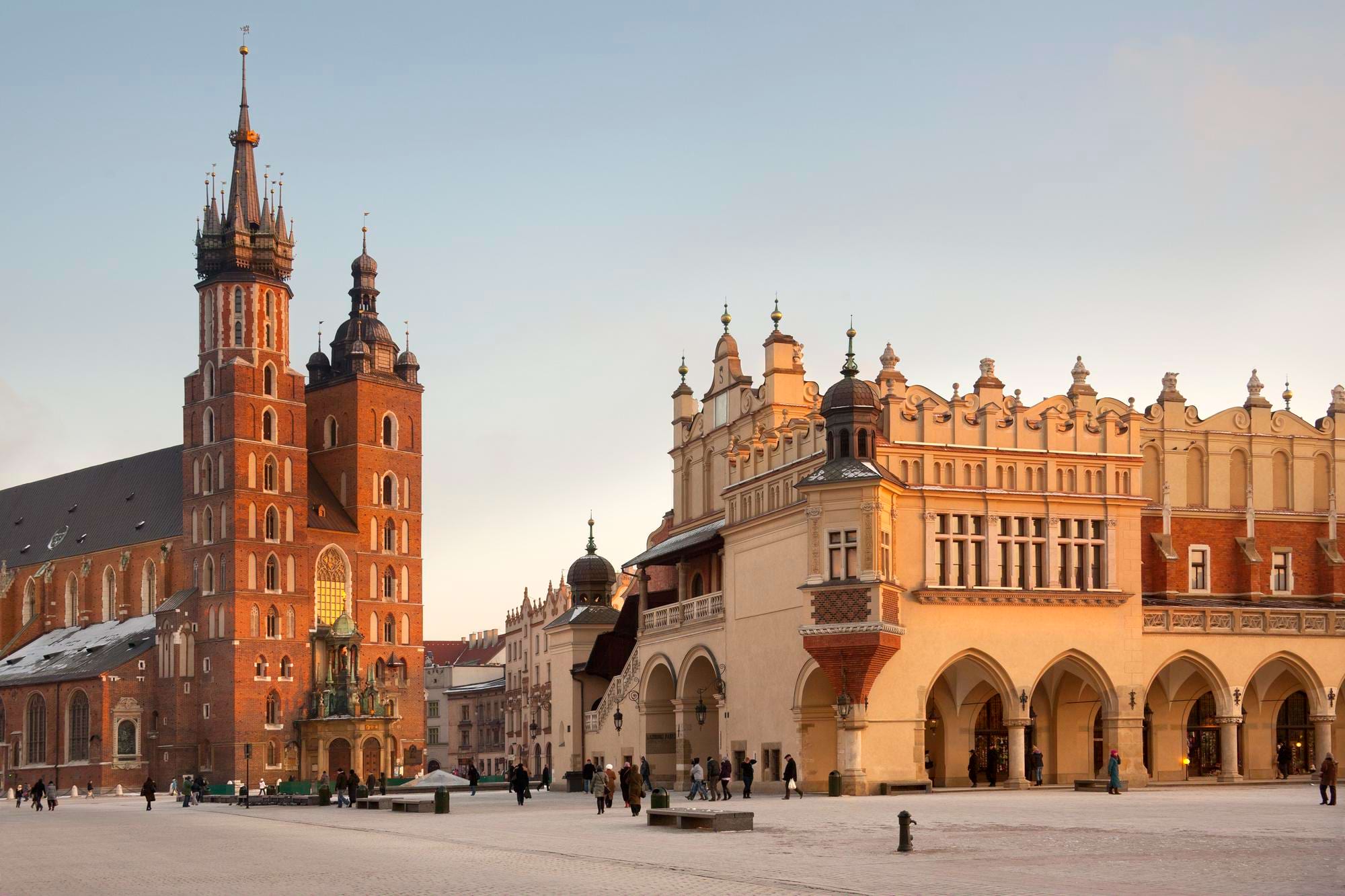Rynek z zabytkową bazyliką i sukiennicami, w ciepłym świetle, z przechodniami na placu