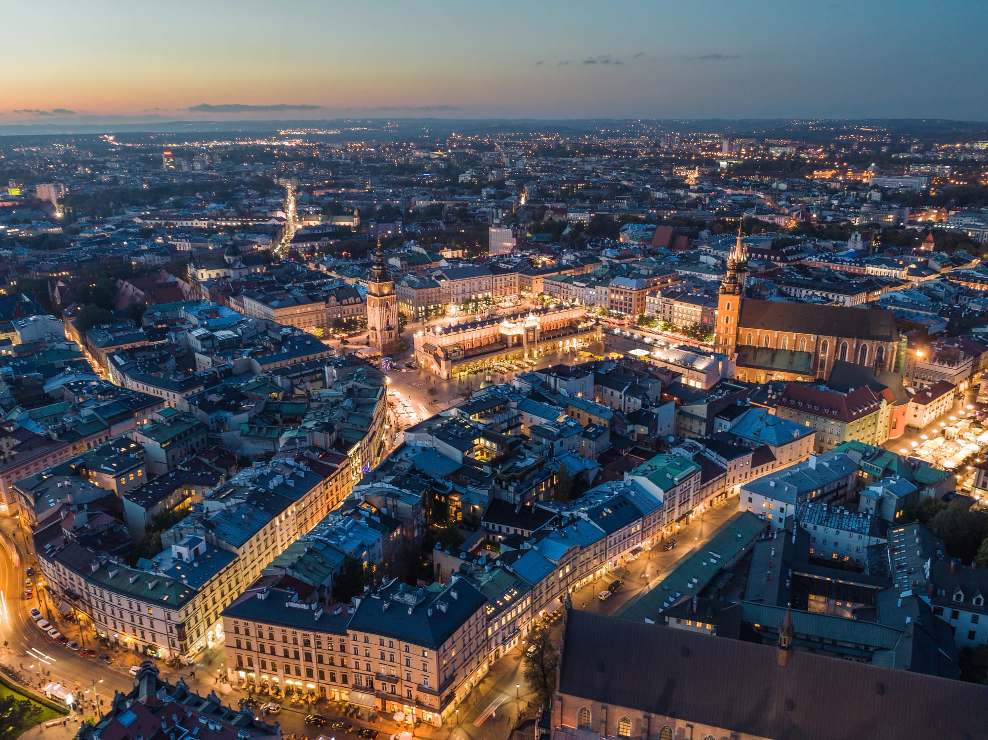 Wieczorna panorama Krakowa z rynku, oświetlone kamienice i kościół przy zachodzie słońca